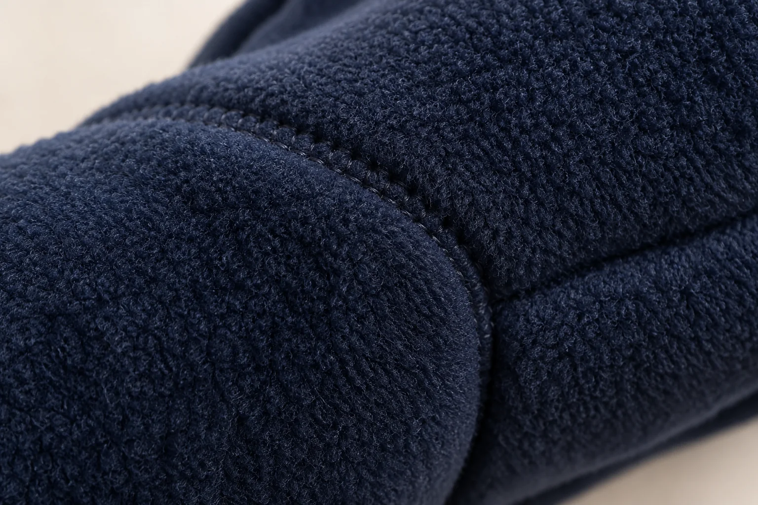 Navy fleece glove: macro on a short curved finger-side join, dense fine navy fleece pile wrapping across adjacent panel.