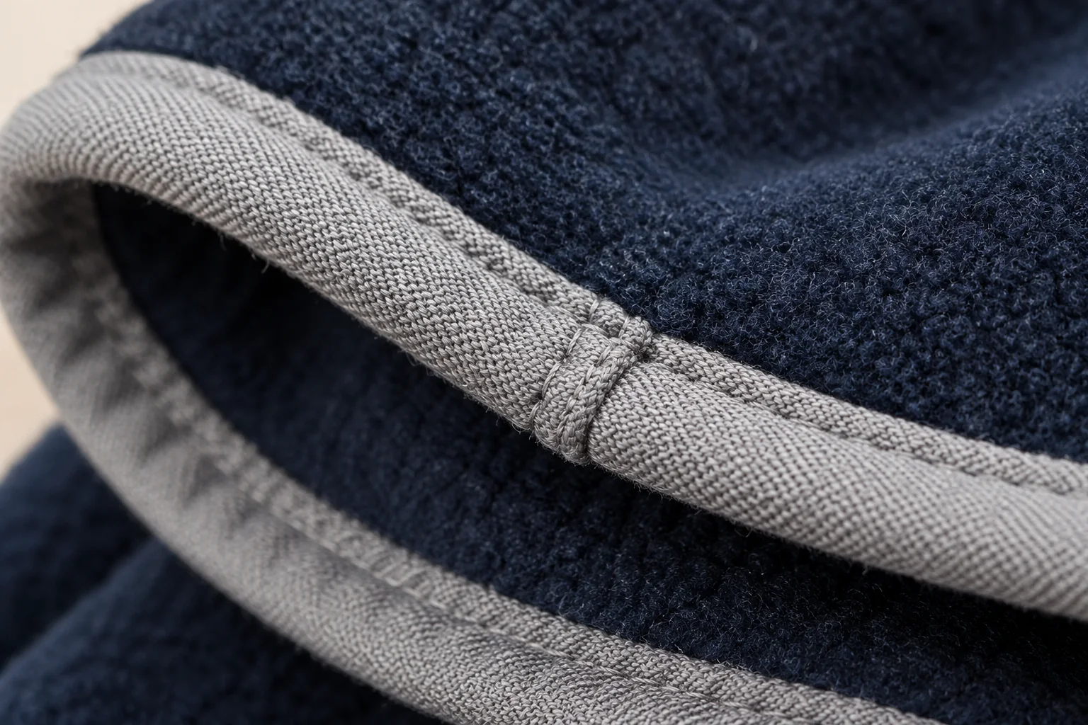 Navy fleece glove: extreme macro of light gray binding around navy cuff edge.