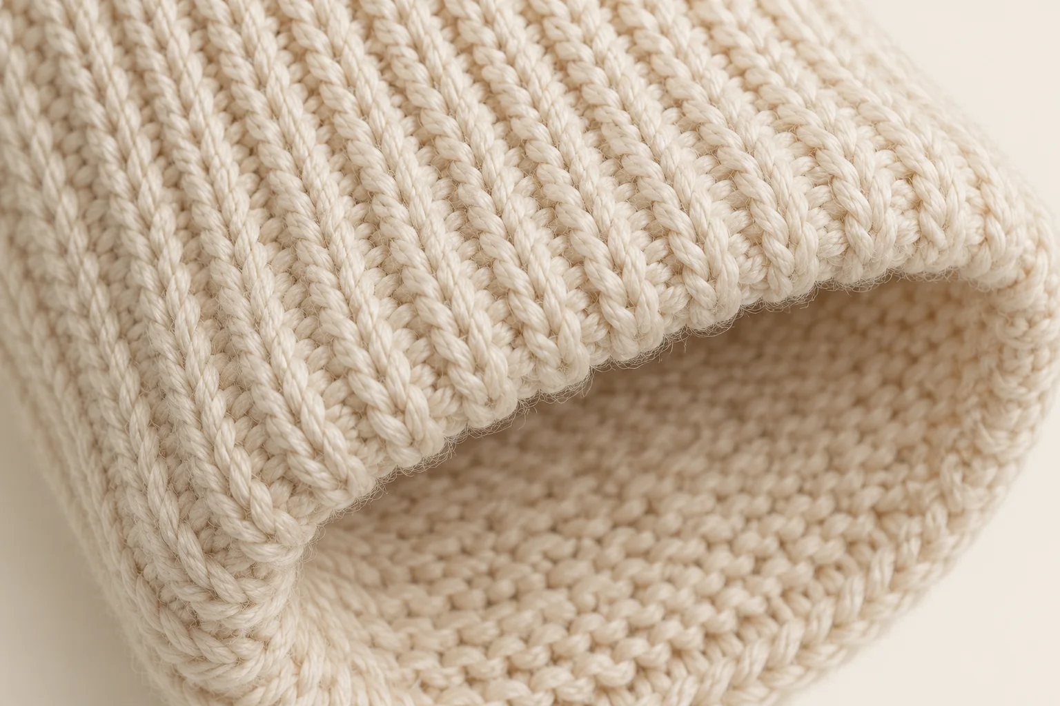 Cream cable-knit glove: macro of a small curved rib cuff rim gently turned enough to reveal cream reverse purl loops on the inside.