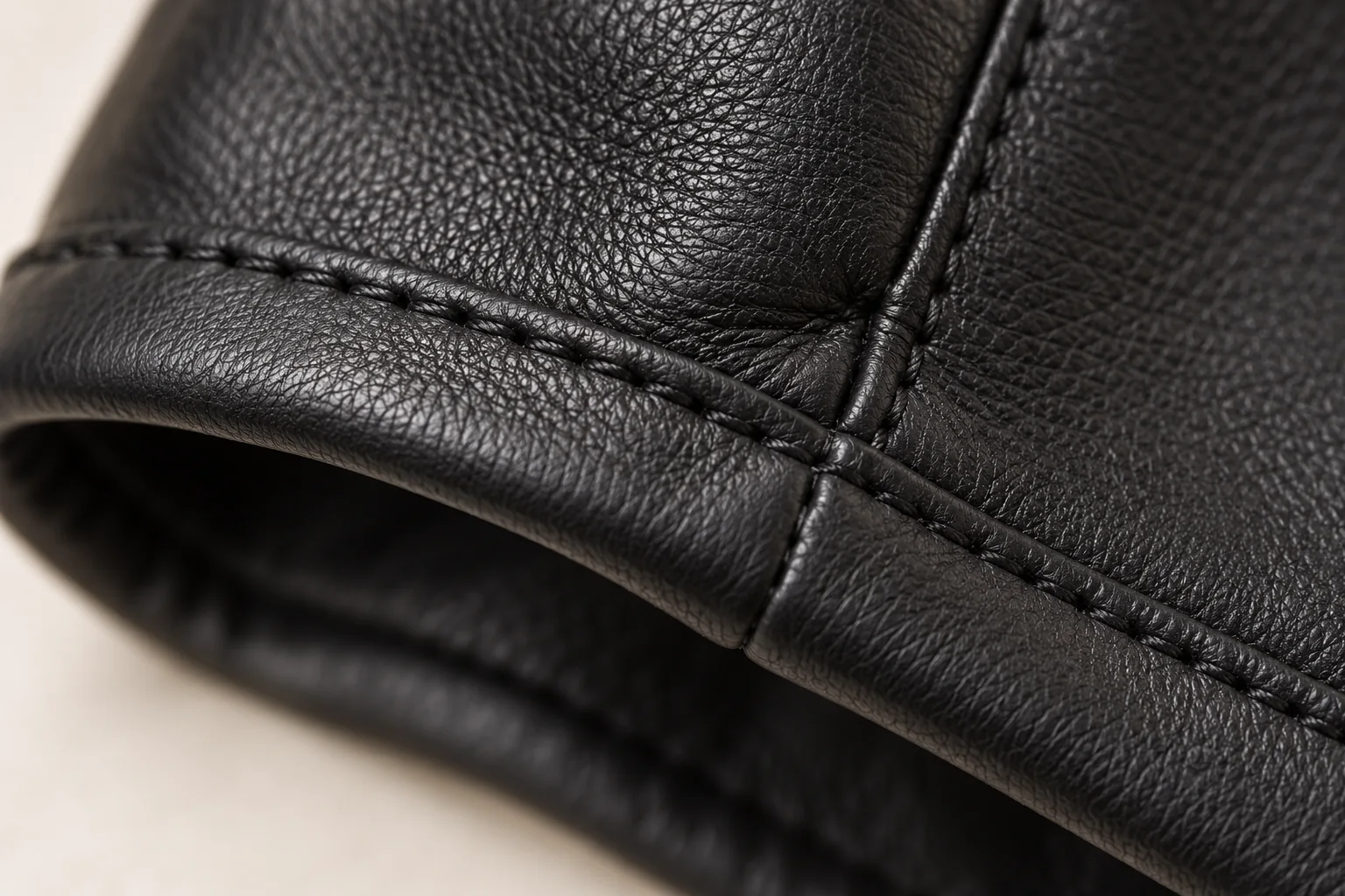 Black leather glove: macro of a narrow turned leather cuff edge with one neat black topstitch line and a side-seam meeting it.