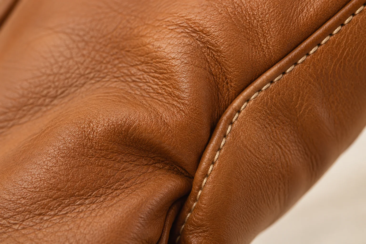 Cognac soft leather glove: macro at a shallow natural bend where hand-back leather turns into a side strip.