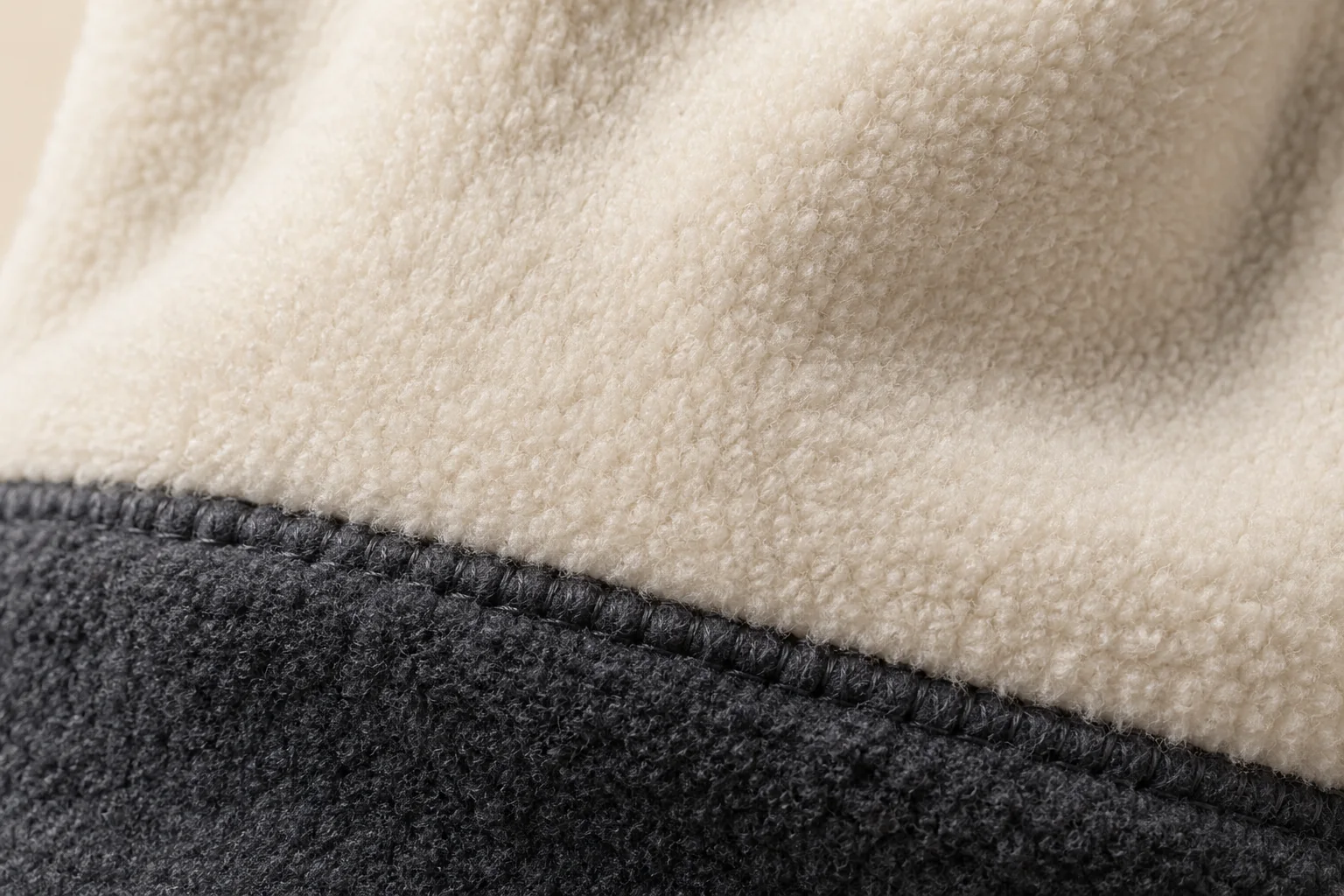 Two-color fleece glove: macro cream hand panel near boundary with charcoal extended cuff.