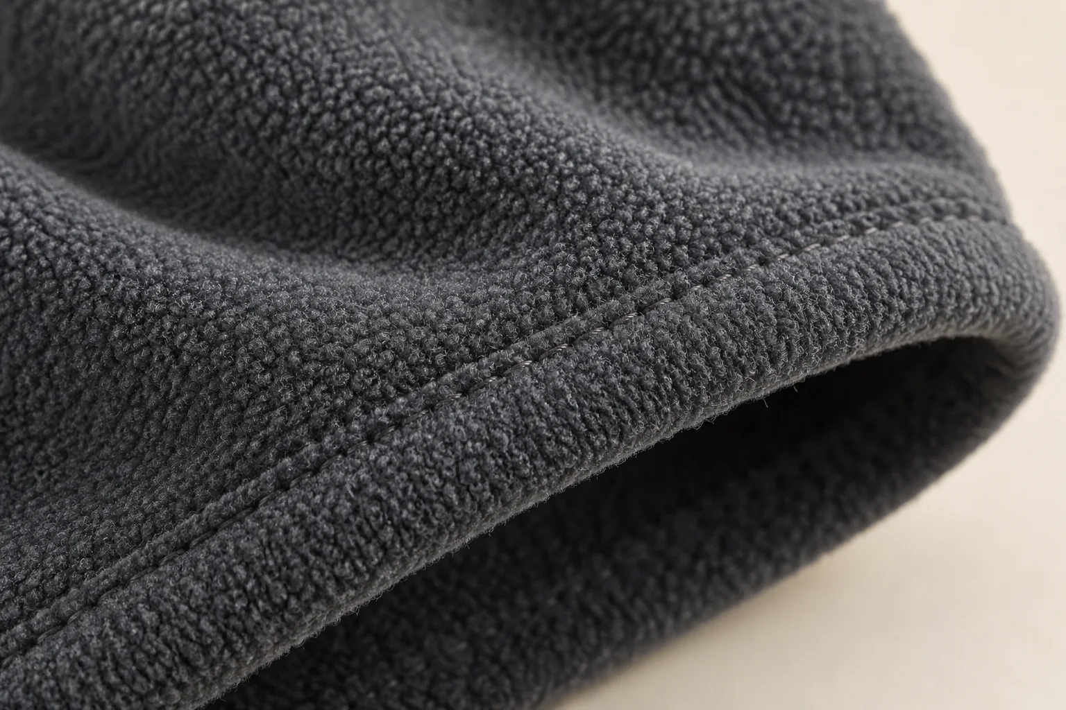 Extended-cuff fleece glove: macro charcoal fleece cuff hem, soft short pile folds around a simple thin turned edge with tonal stitch line.