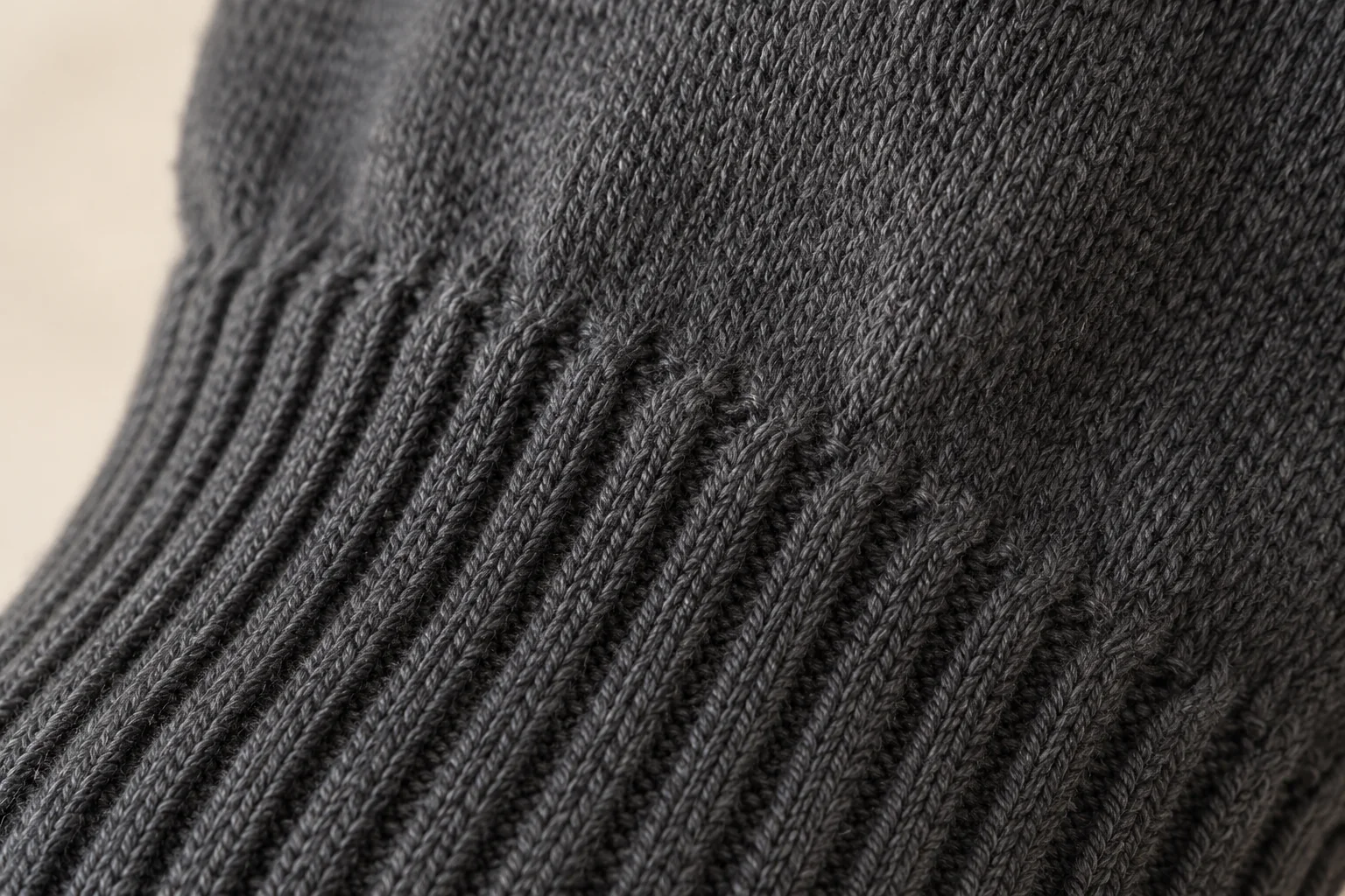 Charcoal knit glove: macro of straight rib cuff joining plain stockinette hand, vertical ribs transform into V loops across wrist curve.