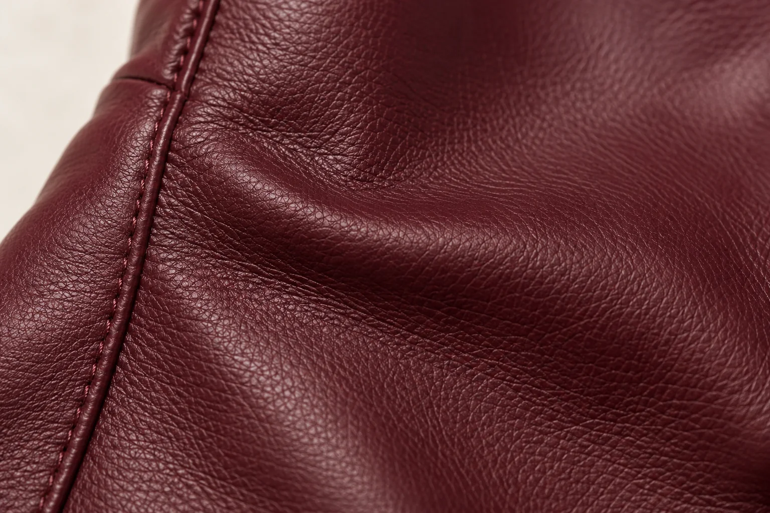 Burgundy leather glove: macro of a shallow natural fold on the extended wrist panel with its slender tonal side seam entering at left.