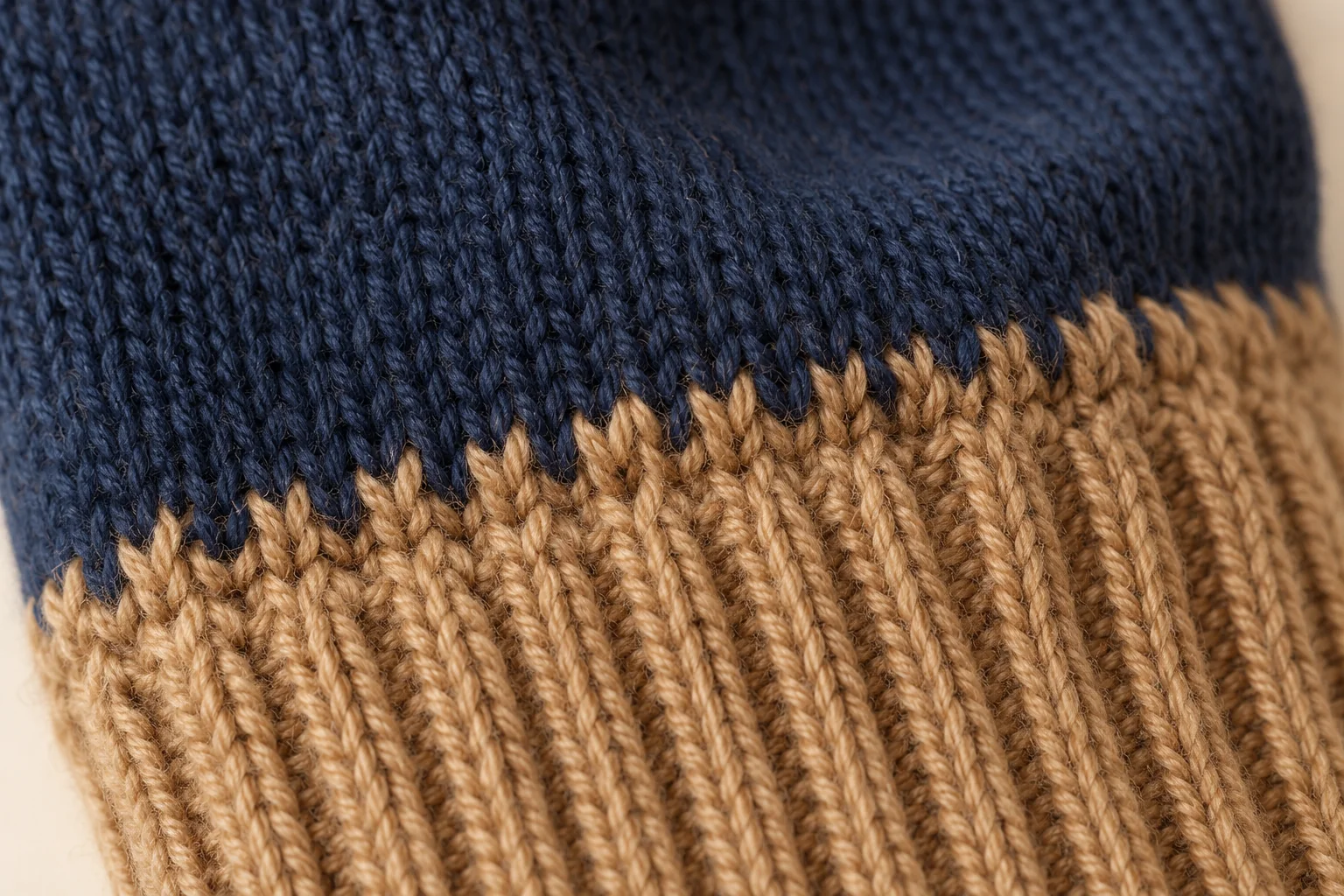 Two-tone knit glove: extreme macro exactly at navy stockinette body to camel vertical-rib cuff color join.