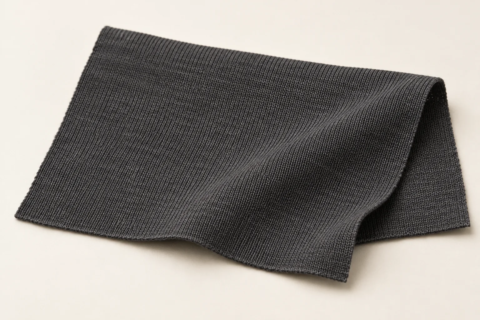 Thin charcoal knit swatch with fine stockinette loops and a soft drape